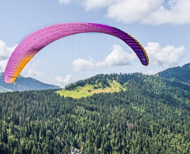 Experience an adventurous paragliding flight over lush alpine landscapes under a vibrant sky.