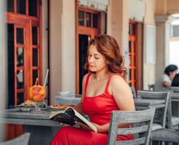Woman in red dress reads at a cafe in Lerma de Villada, Mexico, with a vibrant atmosphere.