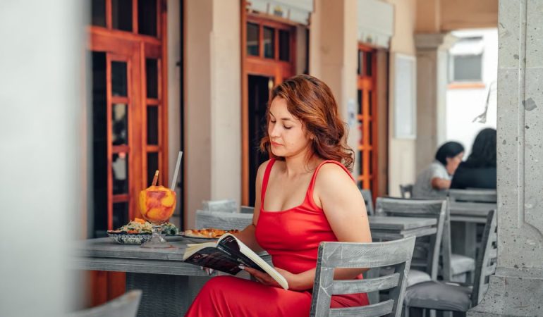Woman in red dress reads at a cafe in Lerma de Villada, Mexico, with a vibrant atmosphere.