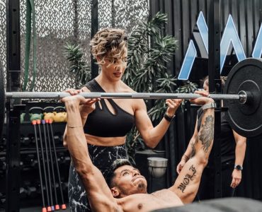 Man lifting weights with woman spotting in Mexico City gym. Urban and dynamic fitness scene.