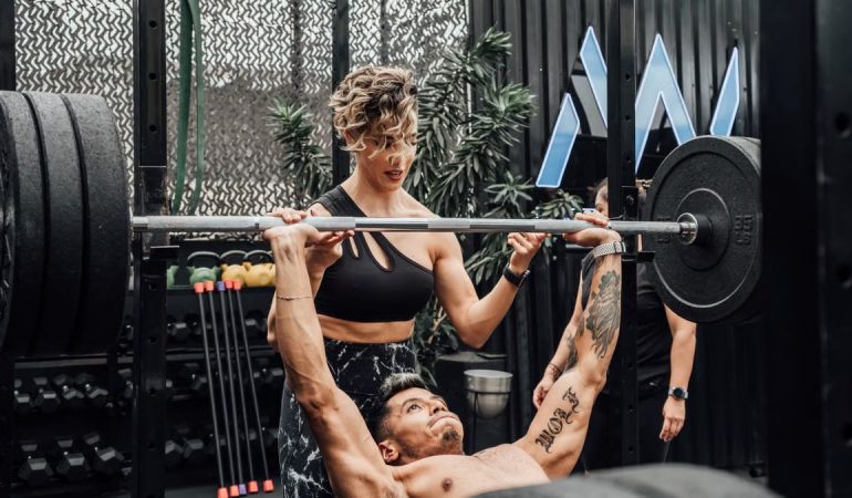 Man lifting weights with woman spotting in Mexico City gym. Urban and dynamic fitness scene.
